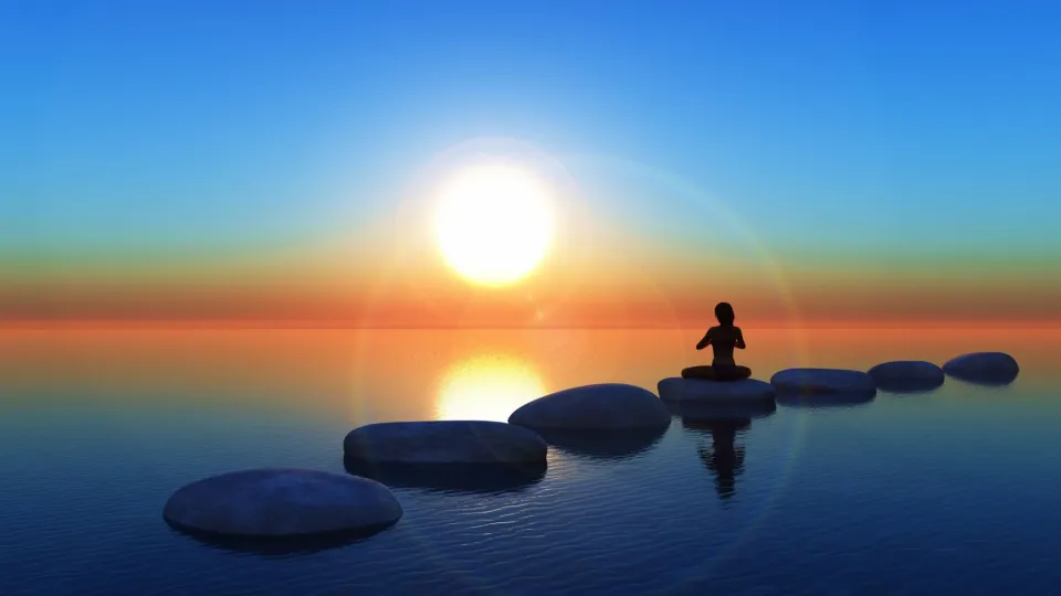 Person Sitting On Large Rocks On A Beach In A Meditative Position