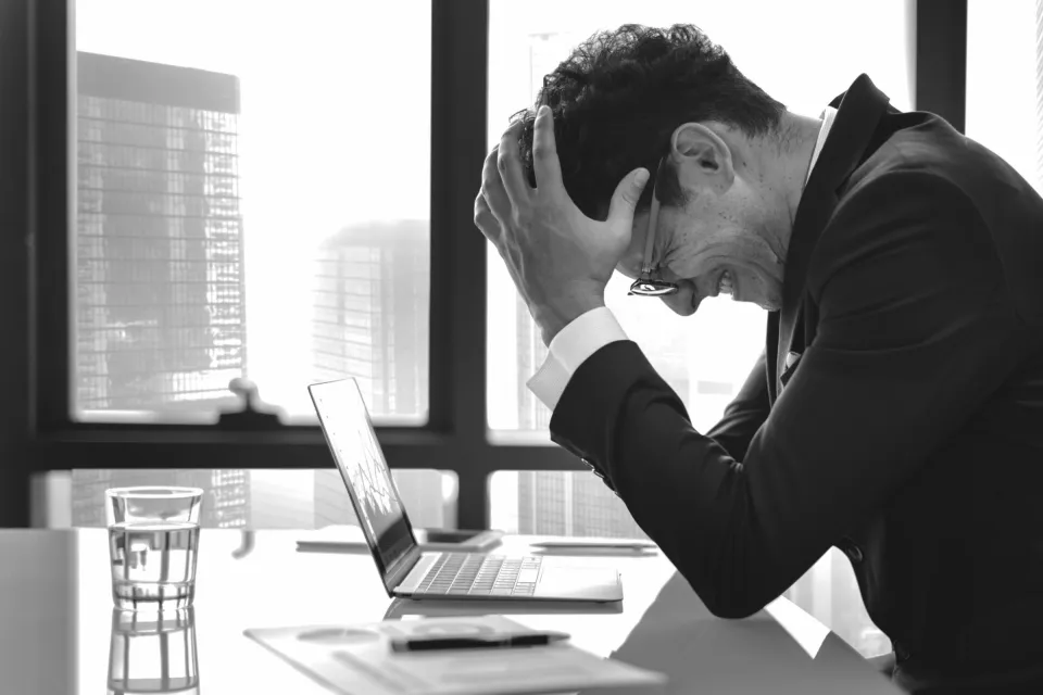Man Sitting At His Desk Holding his Head In His Hands After Realizing That He Made A Huge Mistakes